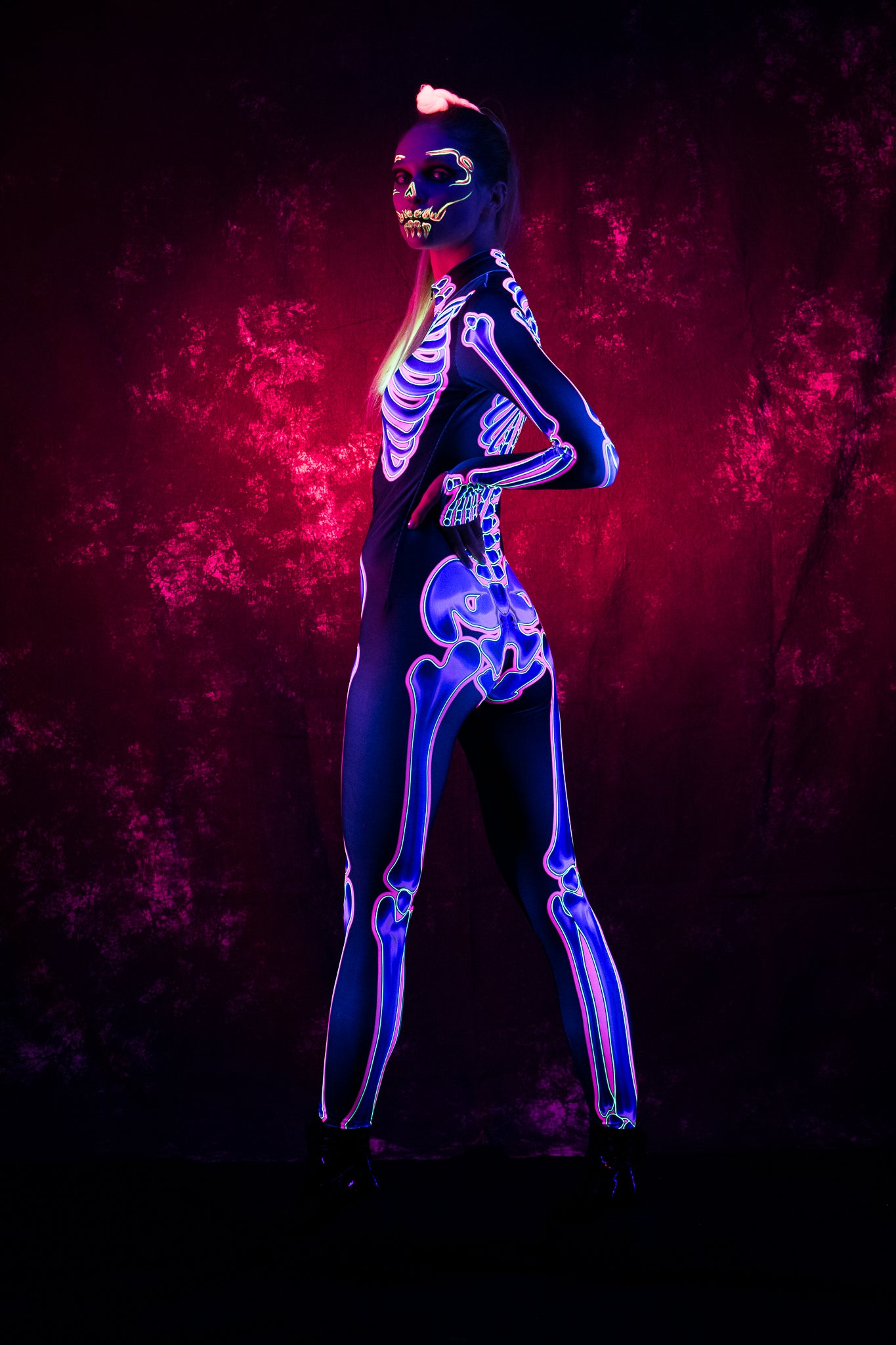 Woman wearing the UV reactive neon pink skeleton costume, a full-body fluorescent jumpsuit perfect for Halloween or rave festivals.