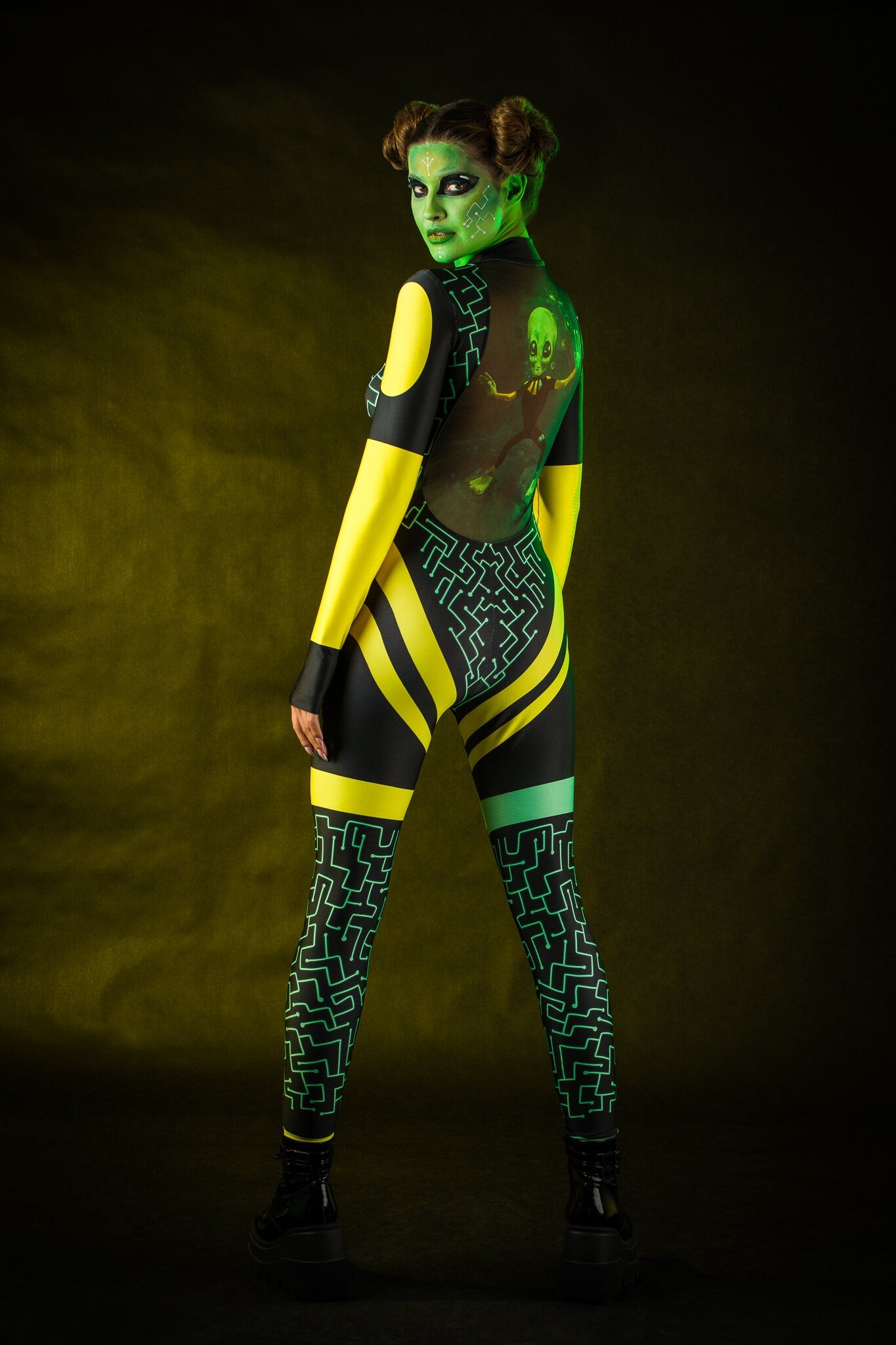 Woman posing in the Green Alien Halloween costume, showcasing the sleek green jumpsuit and tattoo effect, great for Halloween or as a standout festival outfit.